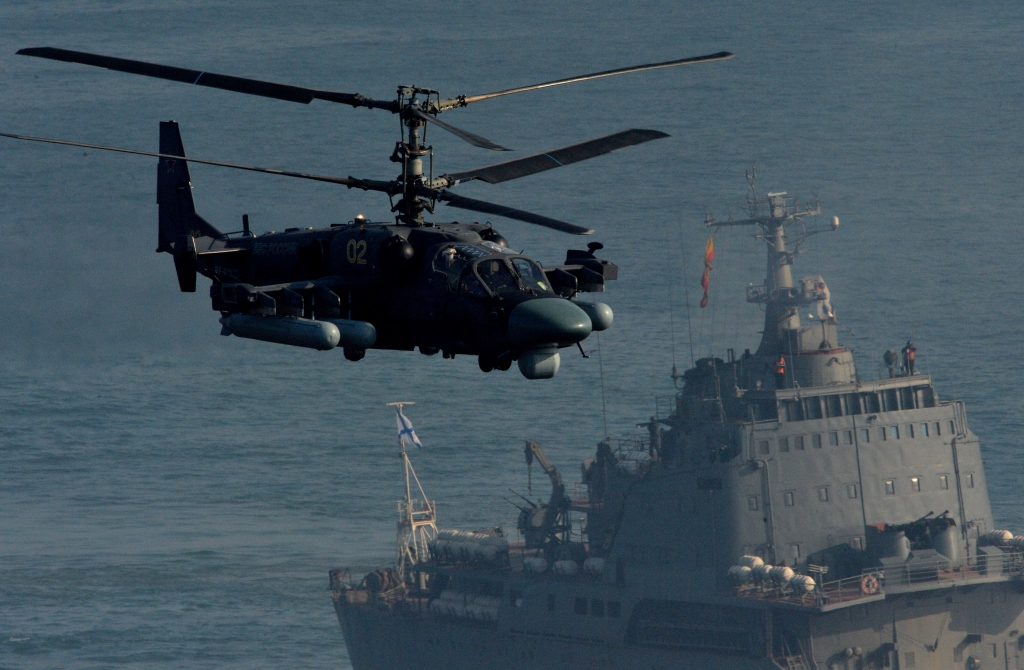 Боевой вертолет Ка-52 проходит над полем боя. На заднем плане виден большой десантный корабль "Николай Вилков"
